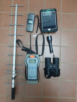 Equipment used to study kinkajous in the wild. Clockwise from left: a radio antenna to pick up signal from kinkajou’s telemetry collars, a radio transceiver to convert radio signal into beeps audible to humans, an iPad mini for collecting behavioral data and recording observations, a low frequency (red) flashlight, binoculars, and a base-station for downloading data from the telemetry collars using the radio signal.